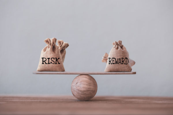 Risk and reward bags on a basic balance scale in equal position on wood table. risk management concept, depicts investors use a risk-reward ratio to compare the expected return of an investment